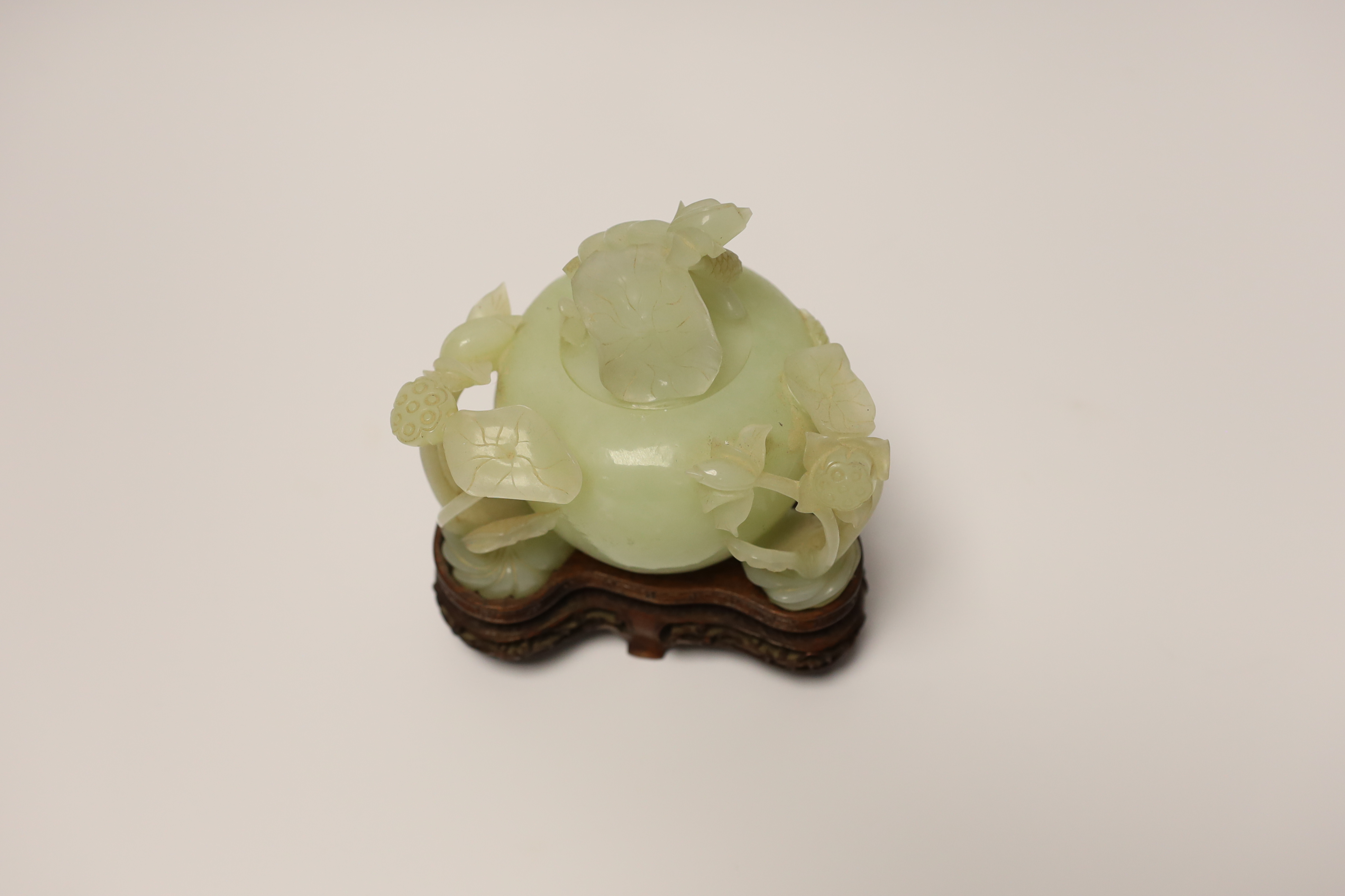 A Chinese carved bowenite jade ‘lotus’ water pot and cover on hardwood stand, 13cm